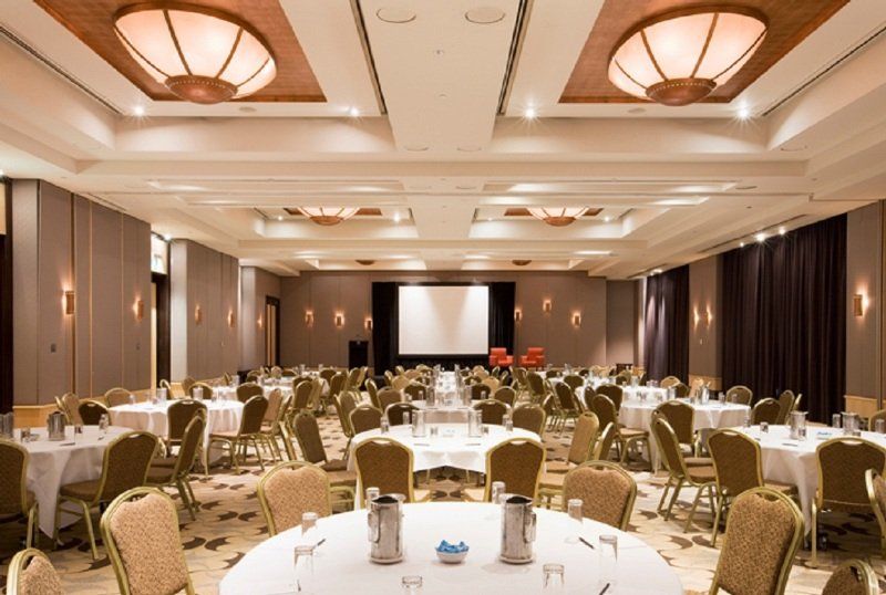 Amora Hotel Jamison Σίδνεϊ Εξωτερικό φωτογραφία The photo shows a large banquet or conference room. There are several round tables arranged throughout the space, each covered with white tablecloths. The tables are set with water pitchers and glasses. In the center of the room, there is a projectio